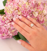 Woman wearing diamond engagement ring and wedding band over a bouquet of pink hydrangea flowers