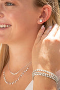 woman holding hand to neck wearing diamond necklaces, bracelets, and earrings