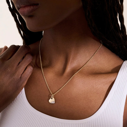 Woman wearing a yellow gold heart pendant with diamonds